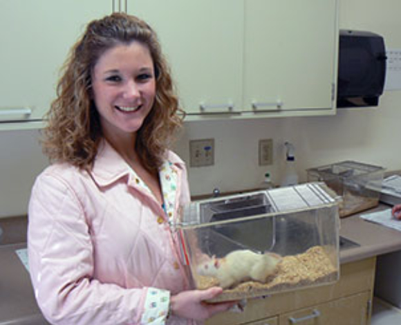 A Mercer University student holds a cage containing a lab rat.