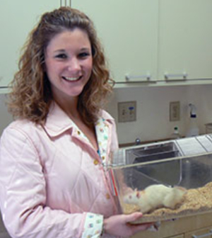 A psychology student holds a cage with a rat in it.