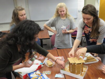 four latin club students build a gingerbread house out of graham crackers and frosting