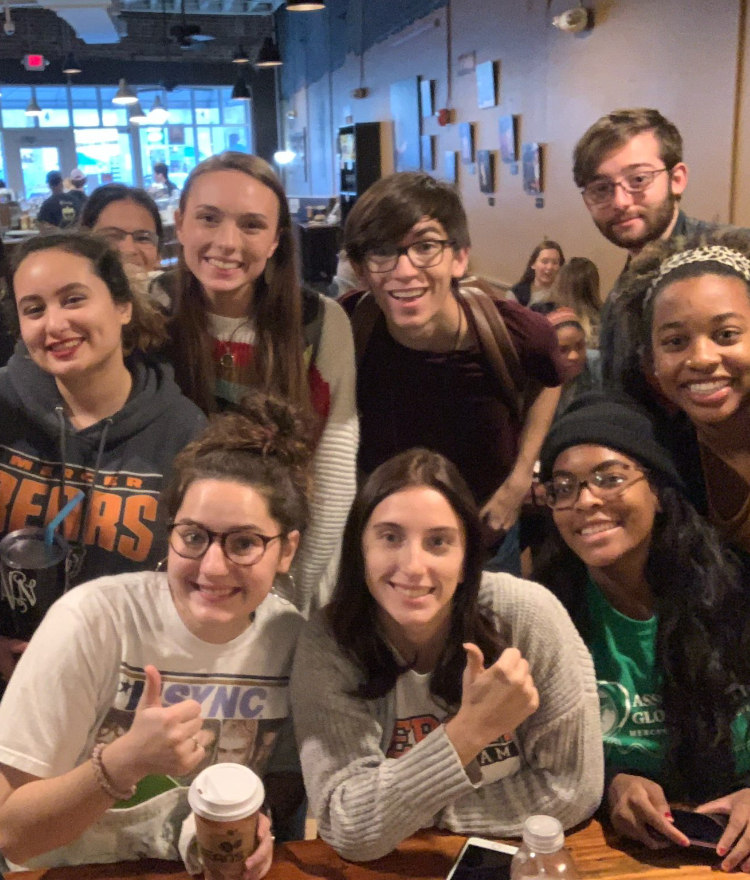 a big group of students gathered in a coffee shop smile for the camera