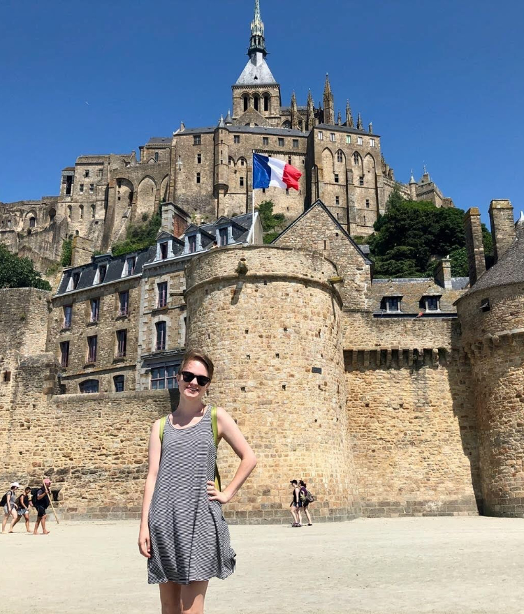 a student poses in front of a castle bearing a French flag