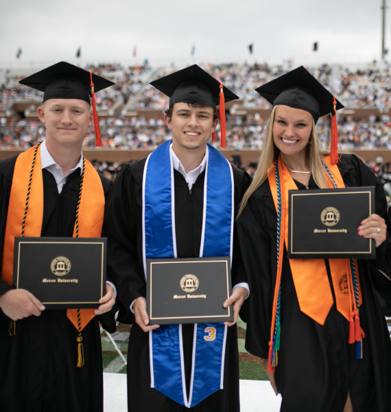 three grads in caps and gowns hold diplomas