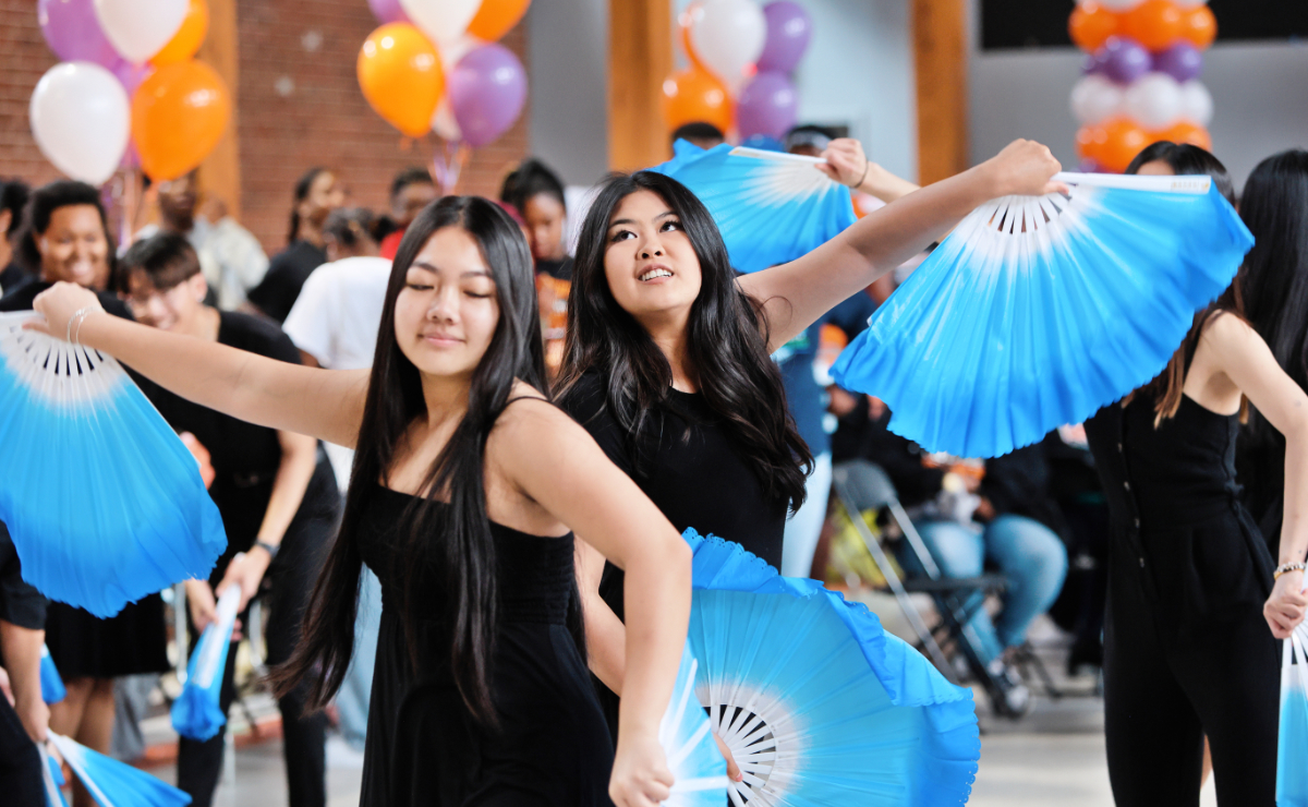 Two women perform a Chinese fan dance with bright blue folding fans.