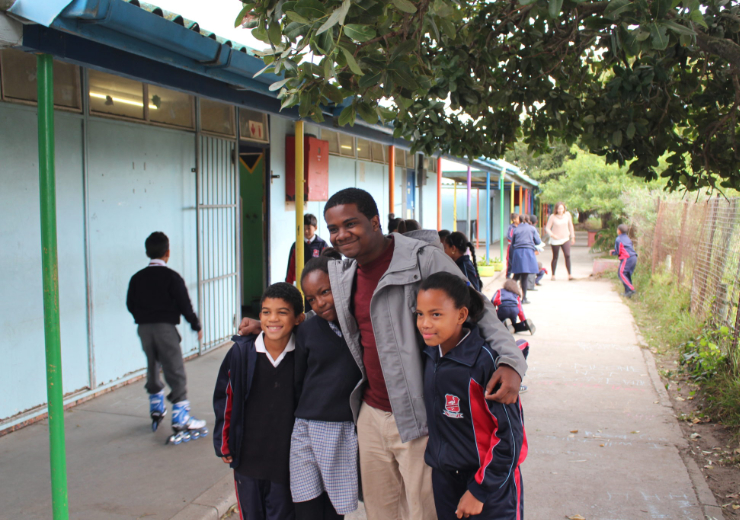 A Mercer student wraps his arms around three schoolchildren. A brightly colored building is in the background.