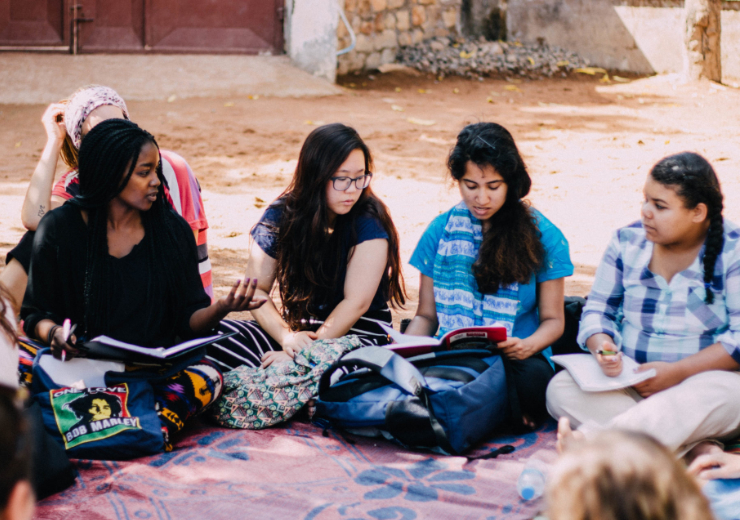 Mercer students sit in a circle on a colorful blanket on the ground in Tanzania.