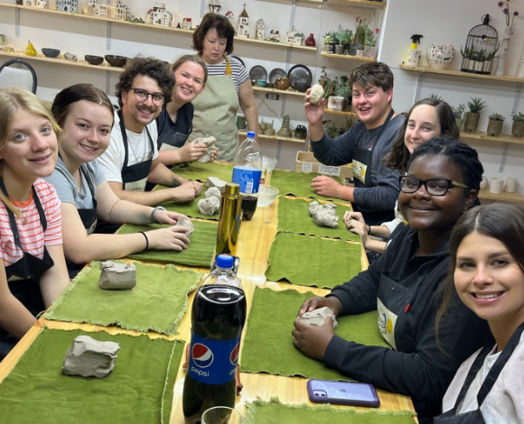 Eight Mercer students sit at a table while working with clay.