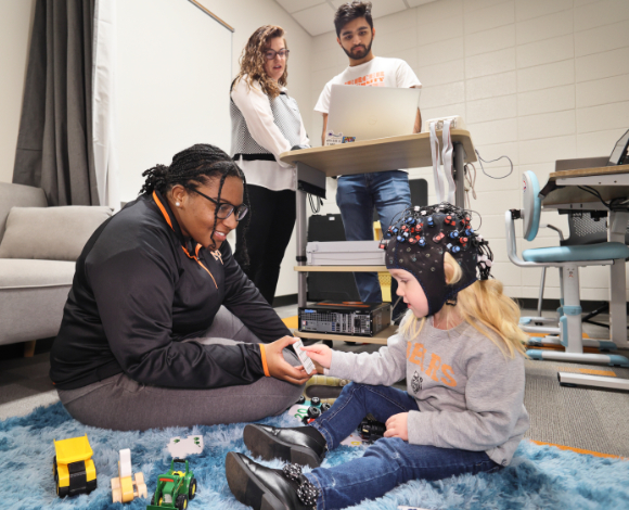 A Mercer student works with a child wearing a cap with wires on it while two people look on.