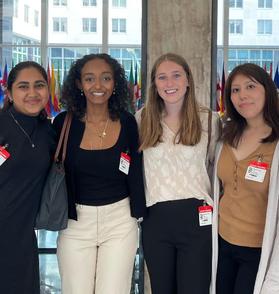 Four Mercer students pose for a photo in a glass building. Various countries flags can be seen behind them.