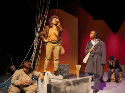 Mercer Theatre actors perform a scene from Men on Boats on a dramatic stage set with ropes, painted waves, and colorful lighting.