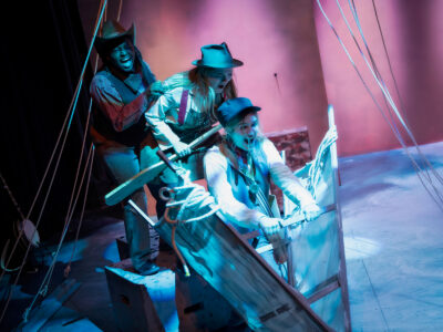 Three Mercer Theatre actors in period costumes shout and struggle with oars and ropes on a prop boat during a dramatic scene in Men on Boats.