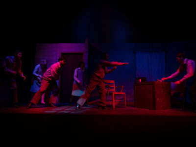 Mercer Theatre actors perform a tense confrontational scene in Grand Guignol, dramatically lit in deep red and blue on a sparse stage set.