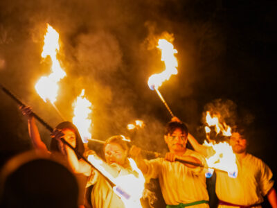 Mercer Theatre performers in white costumes wield flaming batons during a dramatic outdoor night performance of Dragon's Dream.