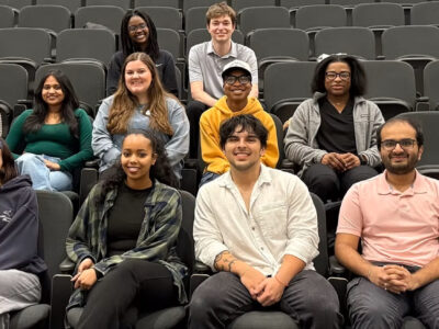 Thirteen students sit in an auditorium.