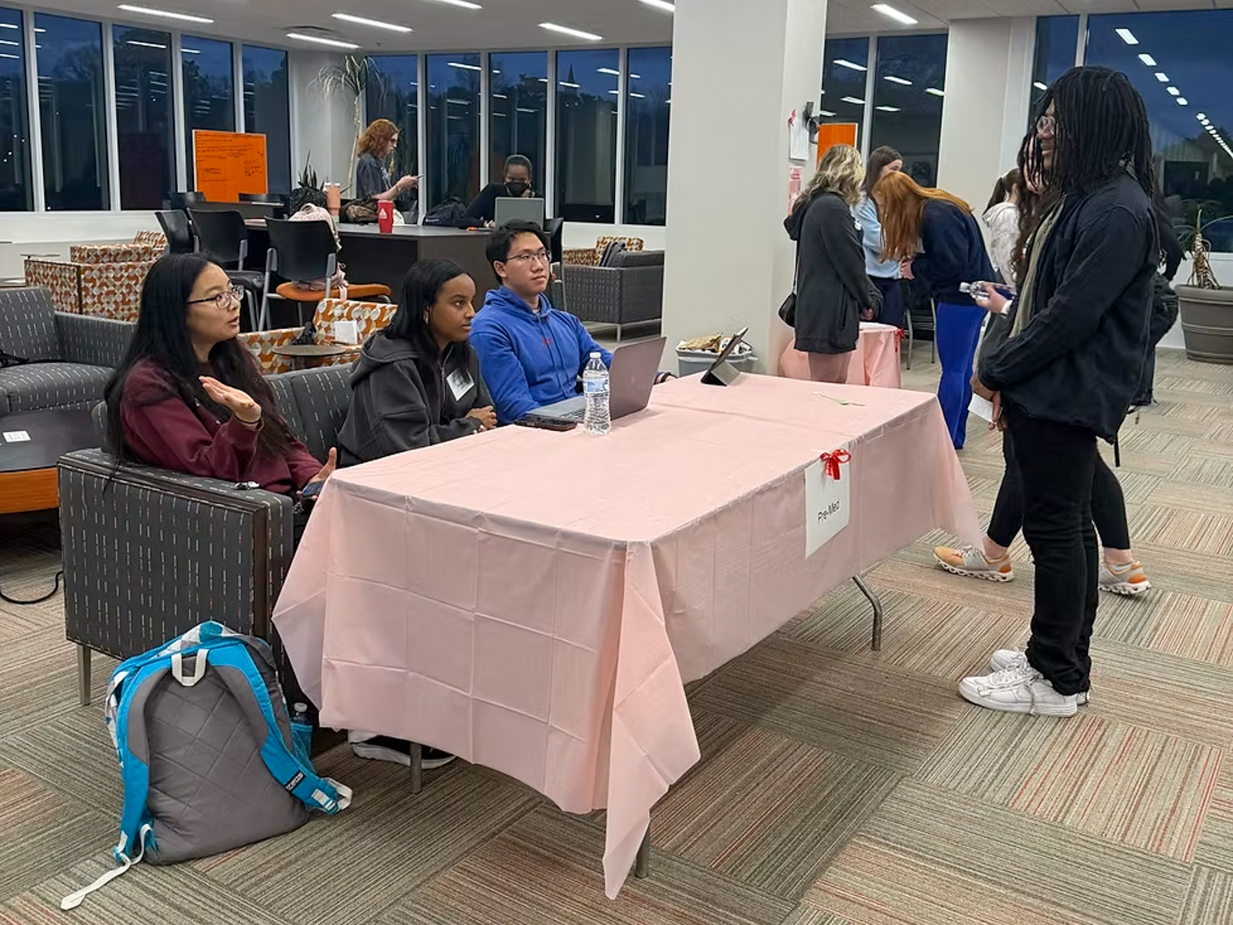 A student conversing with three other students seated at a table labeled pre-med.